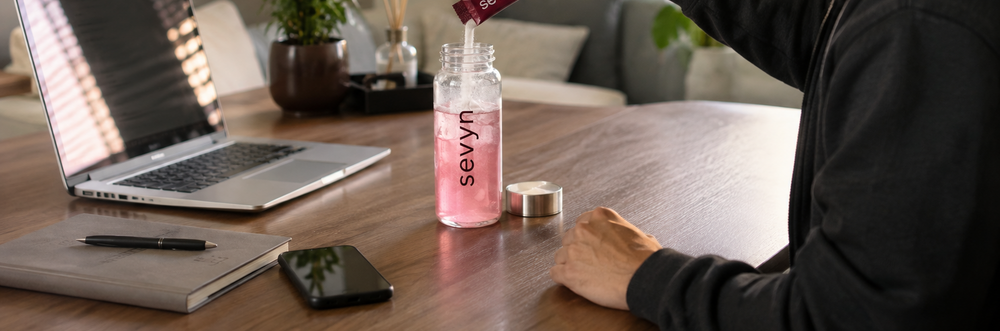 Pouring into a tumbler at a desk — wide shot